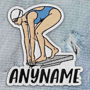 May include: Embroidered patch featuring a swimmer in a blue swimsuit, poised on a diving block. The patch has a white border and the text "ANYNAME" in black, stylized letters. The patch is on a light blue denim background.