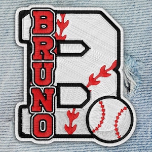 May include: Embroidered patch featuring a large white letter "B" with the name "BRUNO" in red block letters. A baseball is in the lower right corner. Red stitching details and a black border complete the design.