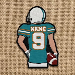 May include: Embroidered patch of a football player in a teal jersey with the number 9 and the word "NAME". The player is wearing a white helmet and holding a football. The patch is outlined in black.