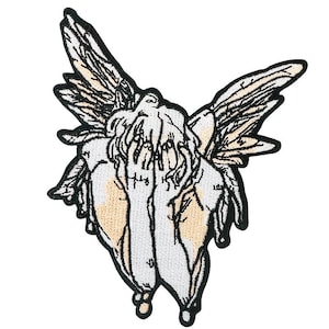May include: Embroidered patch featuring a stylized angel with outstretched wings. The design uses black, white, and tan colors, with detailed linework defining the angel's form. The patch has a black border and is likely for application on clothing or accessories.