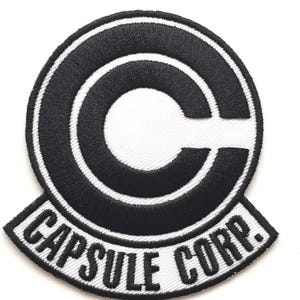 May include: Embroidered patch featuring the Capsule Corp. logo from the Dragon Ball series. The patch has a black and white color scheme, with the text "CAPSULE CORP." at the bottom. The design is circular with a stylized "C" in the center.