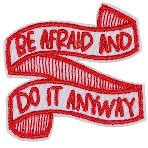 May include: Embroidered patch with the words "BE AFRAID AND DO IT ANYWAY" in red on a white background. The text is in a bold, sans-serif font, and the patch has a ribbon-like design.