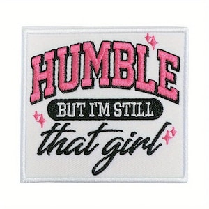 May include: Embroidered patch with the words "HUMBLE" in pink, outlined in black, above "BUT I'M STILL" and "that girl" in black script. Pink starburst accents are on the white background.