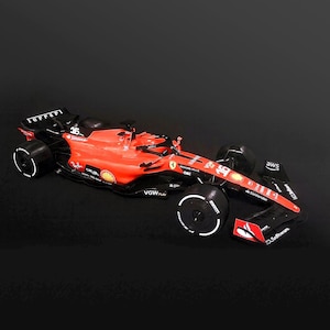 Pode incluir: Um modelo de carro de corrida Ferrari de Fórmula 1 vermelho e preto. O carro apresenta o número 16, logotipos de patrocinadores e detalhes brancos nos pneus. O carro está em um fundo escuro.