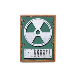 Könnte beinhalten: Rechteckiges Schild mit grünem Hintergrund und silbernem Strahlungssymbol. Das Schild hat einen braunen Rahmen mit abgenutztem Aussehen. Das Wort "CHERNOBYL" ist unten in Silber gedruckt.