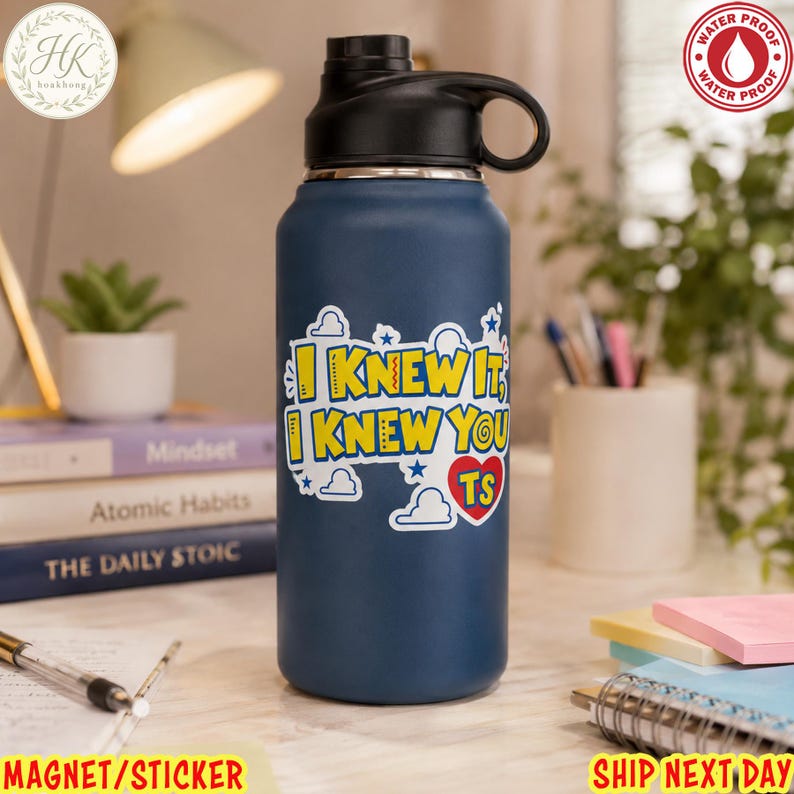 May include: A matte navy blue water bottle with a black screw-top lid and a carry loop. A white sticker on the front features the yellow text I KNEW IT, I KNEW YOU TS with a red heart and blue cloud graphics. The bottle has a waterproof design.
