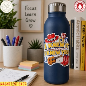 May include: A dark blue metal water bottle with a silver cap, featuring a colorful sticker with a red cowboy hat, alphabet blocks, a guitar, and red cowboy boots. The text on the sticker reads I KNEW IT I KNEW YOU in yellow and blue letters.