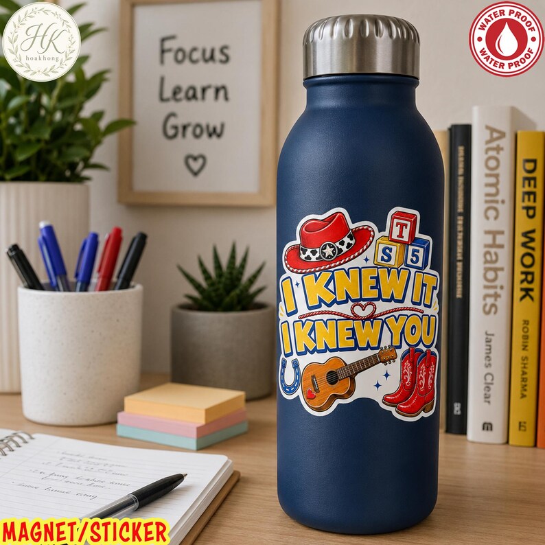 May include: A dark blue metal water bottle with a silver cap, featuring a colorful sticker with a red cowboy hat, alphabet blocks, a guitar, and red cowboy boots. The text on the sticker reads I KNEW IT I KNEW YOU in yellow and blue letters.