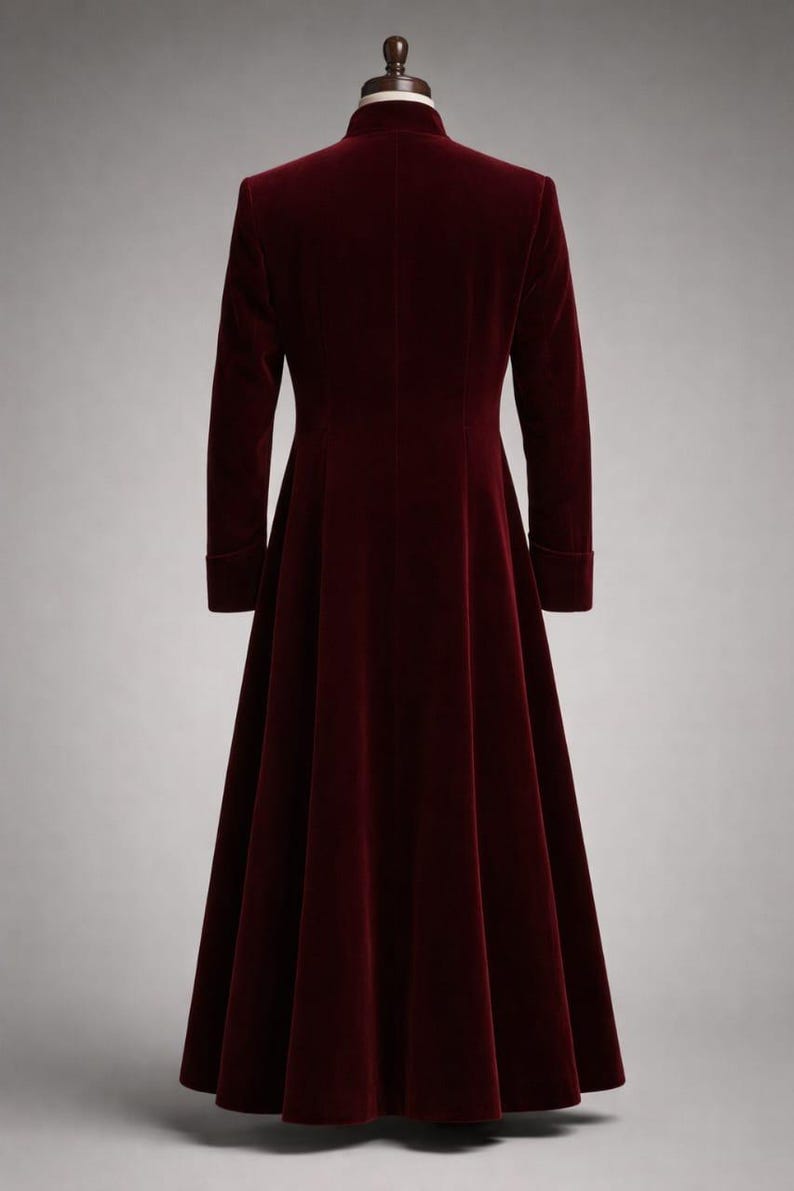May include: A long, burgundy velvet coat with a high collar and long sleeves. The coat has a flared skirt and is displayed against a neutral background. The fabric appears soft and luxurious.