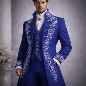 May include: A three-piece royal blue suit with intricate silver embroidery. The suit includes a long coat with ornate button details, a vest, and matching trousers. The ensemble features a high collar and a white ruffled shirt.