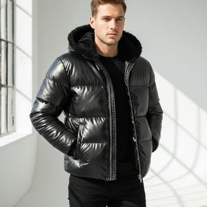 May include: A black puffer jacket with a faux fur-lined hood. The jacket has a shiny, quilted appearance and a full-length zipper. The model is wearing a black shirt and black pants. The jacket has two side pockets.