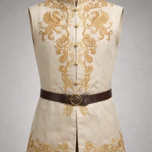 May include: Cream-colored vest with intricate gold embroidery featuring mythical creatures and floral patterns. The vest has a mandarin collar, a row of gold buttons, and a brown leather belt with a gold buckle. A unique garment.