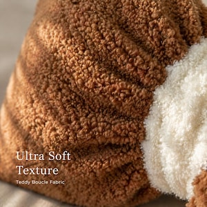 May include: Close-up of a brown teddy boucl&eacute; fabric with an ultra-soft texture. A section of white fabric is visible on the right side. The image highlights the texture of the fabric.