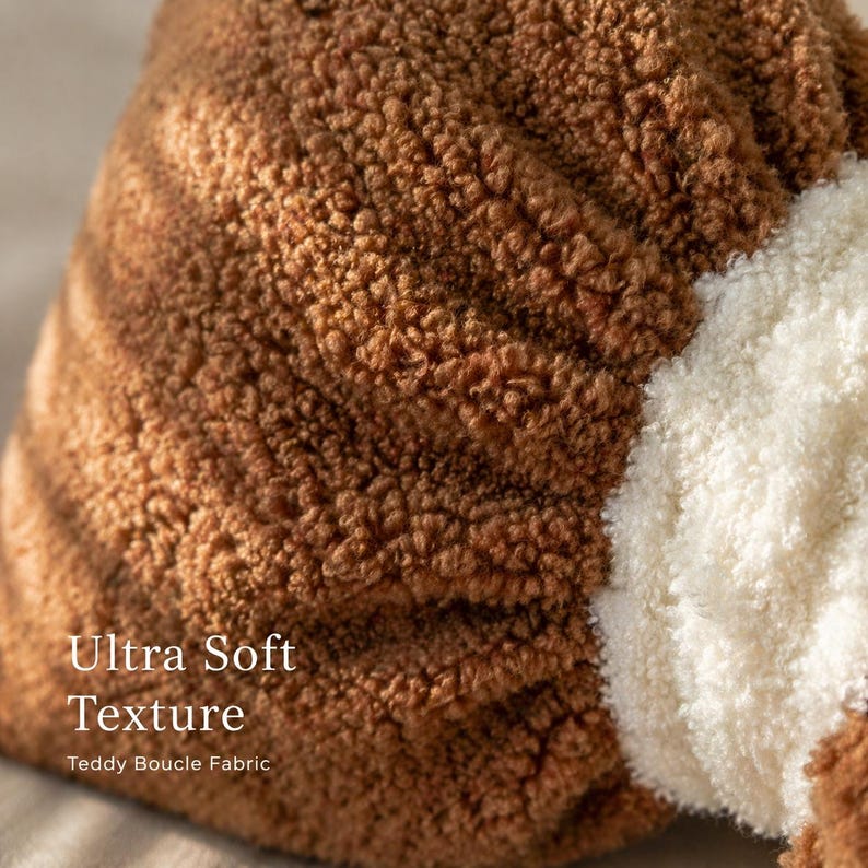 May include: Close-up of a brown teddy boucl&eacute; fabric with an ultra-soft texture. A section of white fabric is visible on the right side. The image highlights the texture of the fabric.