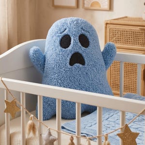 Pode incluir: Um brinquedo de pel&uacute;cia em forma de fantasma azul-claro com uma superf&iacute;cie texturizada semelhante a l&atilde; encaracolada. A pel&uacute;cia apresenta dois grandes olhos pretos ovais e uma boca preta oval menor, todos costurados na parte frontal do objeto.