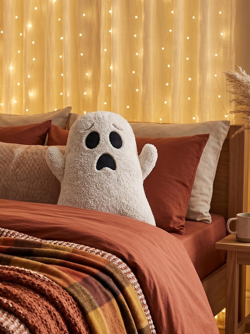 Pode incluir: Uma almofada de pel&uacute;cia em forma de fantasma, na cor branco-sujo, com uma superf&iacute;cie texturizada semelhante a l&atilde; de carneiro. O fantasma apresenta olhos ovais pretos bordados e uma boca preta com express&atilde;o de surpresa, com dois bra&ccedil;os.