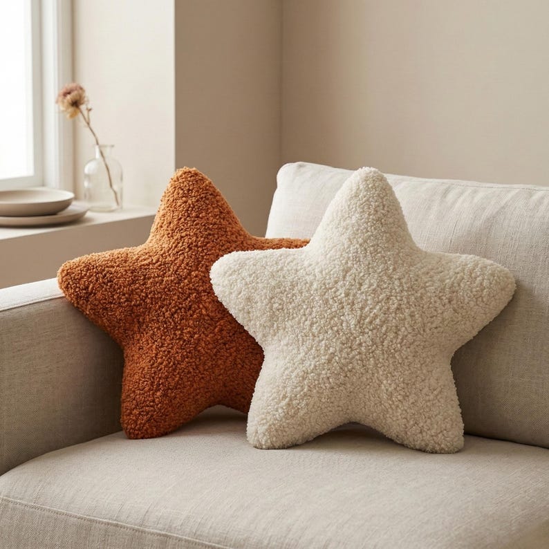 K&ouml;nnte beinhalten: Zwei sternf&ouml;rmige Kissen mit einer strukturierten, lockigen, fleeceartigen Oberfl&auml;che. Ein Kissen ist in einem tiefen gebrannten Orange gehalten, das andere in einem cremigen Off-White. Beide Kissen haben f&uuml;nf Zacken und eine weiche Optik.