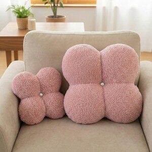 May include: Two pink, four-lobed decorative cushions with a textured, plush surface. Each cushion has a pearl-like button in the centre. The cushions are placed on a beige sofa, creating a cosy and inviting aesthetic.