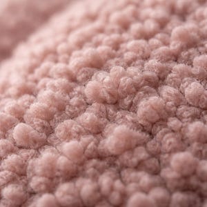 May include: Close-up of a soft, textured fabric in a light pink hue. The material has a plush, bumpy surface, with small, rounded tufts creating a dense, tactile appearance. The overall effect is warm and inviting.
