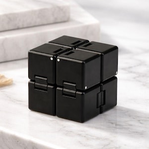Può includere: Un cubo infinito nero, un giocattolo fidget. Il cubo è composto da otto cubi più piccoli collegati da cerniere, che consentono di piegarlo e manipolarlo. La superficie è liscia e riflettente, con piccoli punti bianchi sugli angoli. Il giocattolo è progettato per alleviare lo stress.
