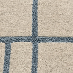 Cream area rug featuring thin blue geometric grid lines and hand tufted construction for Scandinavian interiors in closeup shot