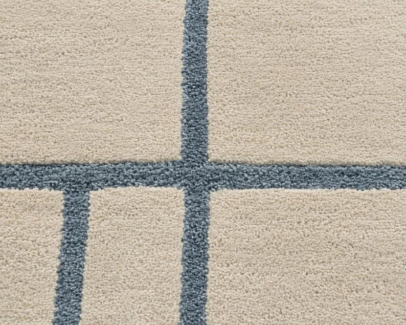 Cream area rug featuring thin blue geometric grid lines and hand tufted construction for Scandinavian interiors in closeup shot