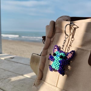 Beaded Stitch bag charm and keychain, handcrafted with purple and turquoise beads. Aesthetic lifestyle shot on a beach boardwalk, unique gift for Disney fans and cute accessory for backpacks or purses.