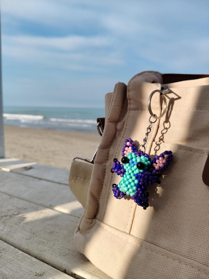 Beaded Stitch bag charm and keychain, handcrafted with purple and turquoise beads. Aesthetic lifestyle shot on a beach boardwalk, unique gift for Disney fans and cute accessory for backpacks or purses.