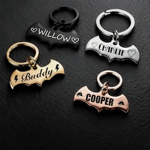 Può includere: Quattro portachiavi in metallo a forma di pipistrello, ognuno con un colore e un design diverso. Uno è nero con "Willow" e cuori, un altro è argento con "Charlie" e cuori, uno dorato con "Buddy" e fulmini e uno oro rosa con "Cooper" e grafiche di topi.