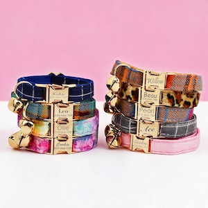 May include: Two stacks of pet collars featuring gold-tone metal buckles engraved with names and phone numbers. The collars display various patterns including plaid, leopard print, and solid colors, each equipped with a small gold-tone bell.