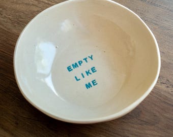 Bol de cerámica neutra con forma orgánica, hecho a mano, con texto azul "VACÍO COMO YO"