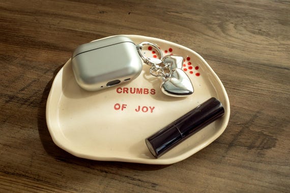 A hand-thrown ceramic dish stamped with 'Crumbs of Joy' that earns its place on a desk or nightstand as a snack bowl, ring dish, and daily mood-lifter all at once.