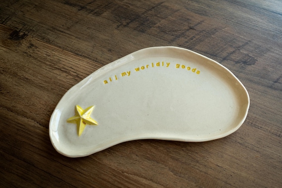A cheerful yellow ceramic star dish stamped with "All My Worldly Goods" — sculptural, quotable, and the kind of handmade piece that feels like a real gift rather than an afterthought.
