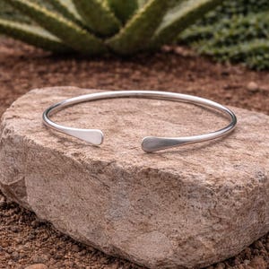 May include: A white ceramic mug with a black handle and the text "But First, Coffee" in a bold, black font. The mug is set against a blurred background, suggesting a cozy setting.