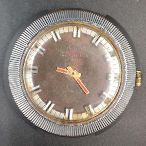 May include: Vintage wristwatch with a brown face, gold hands, and red second hand. The watch has a silver-colored, ridged bezel and a gold-colored crown. The watch face has white rectangular hour markers and the word "CONVA" is printed on the face.