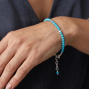 Op de afbeelding: Een delicate armband met turquoise kralen en zilveren accenten. De armband, met zijn helderblauwe kralen, wordt om een pols gedragen. Een sieraad.