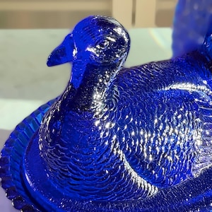 May include: A detailed, close-up of a cobalt blue glass duck figurine. The duck has intricate feather detailing and a textured surface. The figurine is a decorative item, likely for display or collection.