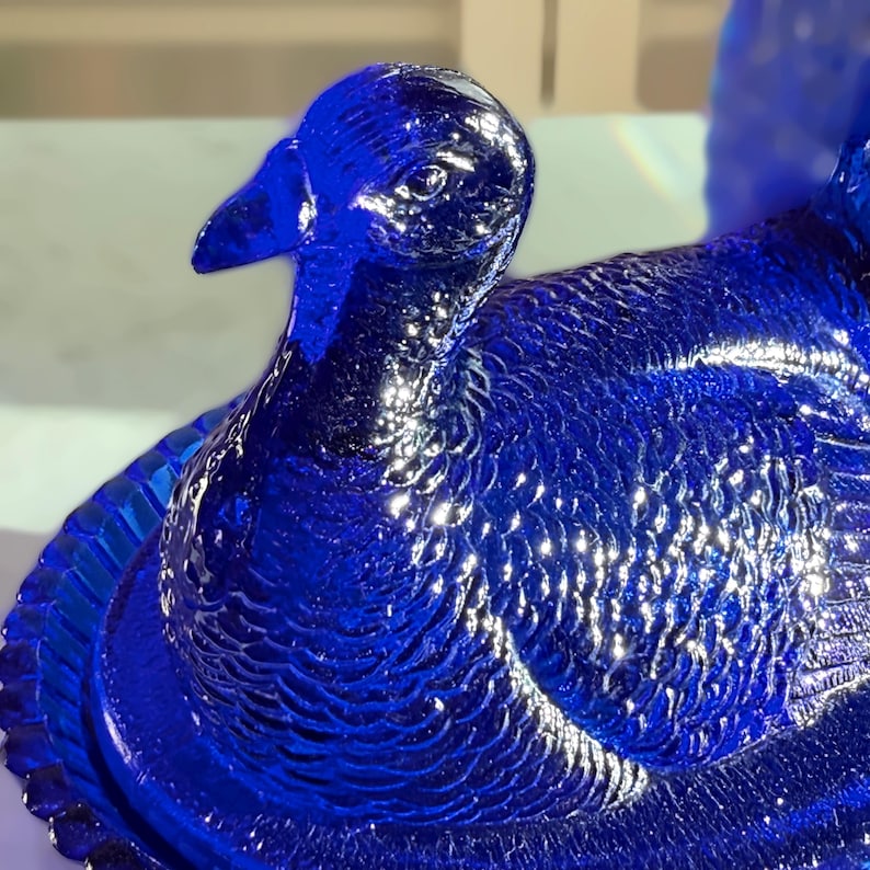 May include: A detailed, close-up of a cobalt blue glass duck figurine. The duck has intricate feather detailing and a textured surface. The figurine is a decorative item, likely for display or collection.