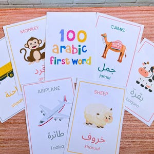 May include: A set of educational flashcards featuring colourful illustrations of a monkey, camel, cow, truck, aeroplane, and sheep. Each card displays the English word, the Arabic translation, and the transliteration. The central card reads 100 arabic first word.