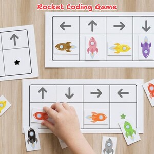 May include: Rocket Coding Game with white rectangular boards featuring black arrow icons and grid spaces. Includes small rectangular cards with colorful rocket illustrations in brown, pink, yellow, purple, red, orange, green, and gray.