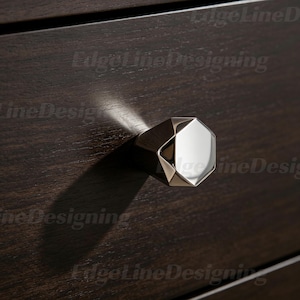 May include: A close-up shot of a modern, geometric cabinet knob with a polished chrome finish. The octagonal knob reflects light, set against a dark wood drawer front. The hardware adds a contemporary touch.