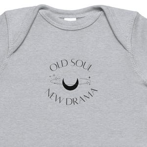 Op de afbeelding: Een lichtgrijze babybody met korte mouwen. De body heeft een zwart grafisch ontwerp met de woorden "OLD SOUL NEW DRAMA" rond een maan en sterren.