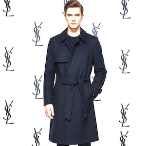 Peut inclure: Un trench-coat bleu marine avec une ceinture assortie, porté sur un pull noir et un pantalon noir. Le manteau a un design classique avec un col à revers et des poches. Le fond présente un motif répété d'un logo.