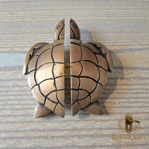 Op de afbeelding: Bronzen schildpadvormige deurgrepen. De handgrepen zijn in tweeën gesplitst, waarbij elke helft van de schildpad een handgreep vormt. Het ontwerp heeft gedetailleerde lijnen en een sleutelgat in het midden. De handgrepen zijn gemaakt van messing en zijn geschikt voor een kust- of nautisch thema.