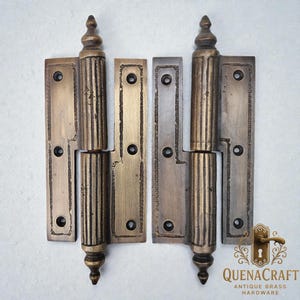 Puede incluir: Dos bisagras antiguas de latón con un diseño acanalado vertical en el cuerpo central y remates decorativos. Cada bisagra tiene una placa rectangular con agujeros para tornillos. Las bisagras son de color latón envejecido.