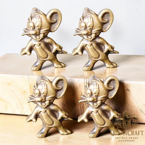 May include: Four brass Jerry Mouse figurines. Each figurine is in a standing pose with arms outstretched and a smiling expression. The figurines are a warm gold color and appear to be antique hardware.