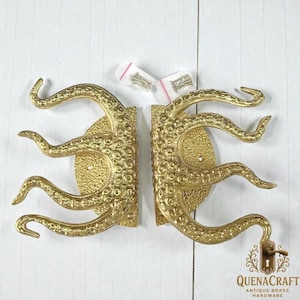 May include: Two brass-colored door handles, each shaped like an octopus tentacle, with a textured surface. The handles are mounted on a textured, circular base. Small hardware packets are visible. The QuenaCraft logo is in the bottom right corner.