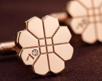 Puede incluir: Un par de gemelos de oro rosa con un diseño en forma de flor de ocho pétalos redondeados. El centro tiene un patrón de cuadrícula y un pétalo está grabado con un pequeño símbolo y una piedra preciosa transparente incrustada.