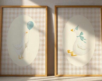 May include: Two framed art prints featuring watercolor illustrations of geese. One goose holds a blue balloon, the other wears a party hat and bow. The background is a light beige oval on a plaid pattern.