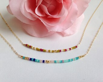 May include: Two gold chain necklaces with colorful beaded accents. The top necklace has red, white, and green beads, while the bottom necklace has blue, turquoise, and pink beads.